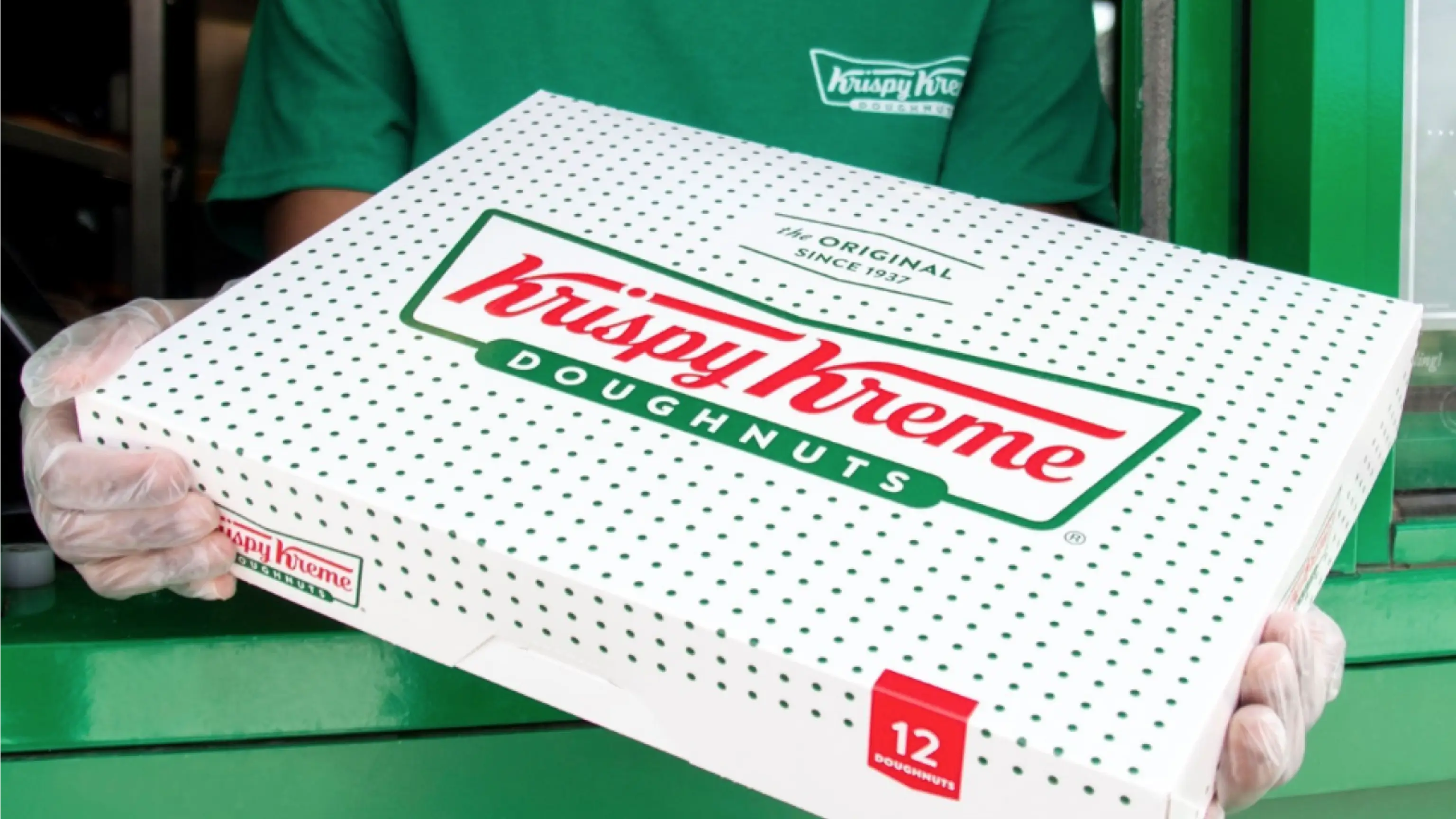 Krispy Kreme drive-thru employee handing box of dozer doughnuts to customer.