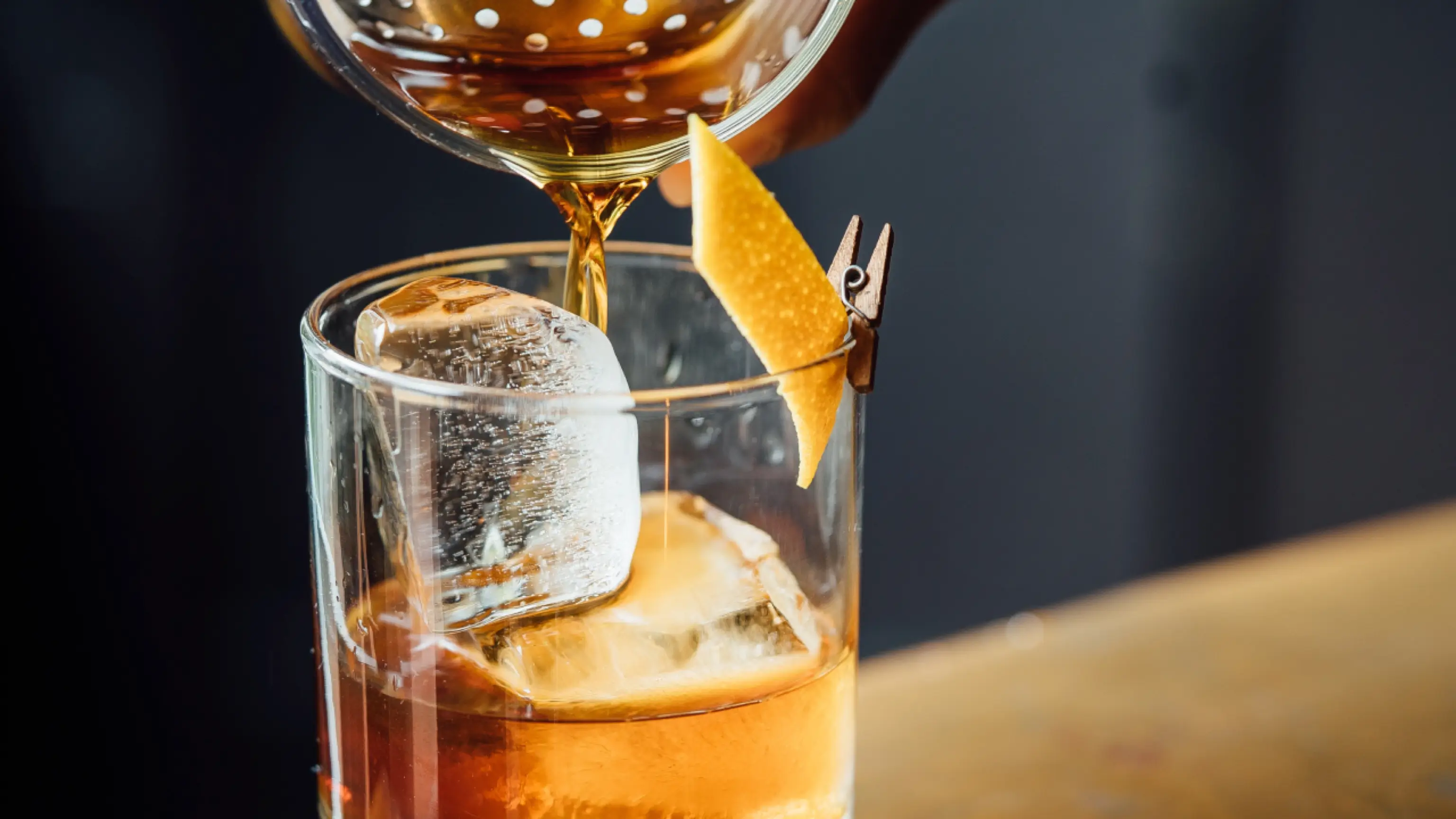Pitcher pouring Sazerac brand Manhattan cocktail into glass with ice and orange slice